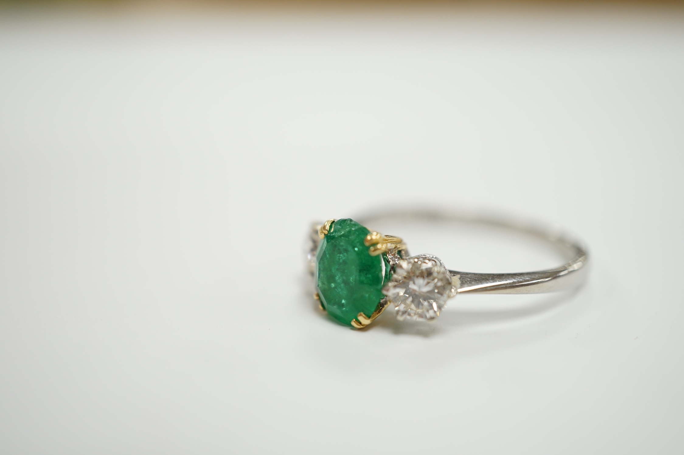 A 1970's 18ct white gold, single stone oval cut emerald and two stone diamond set ring, size P/Q, gross weight 3.2 grams.